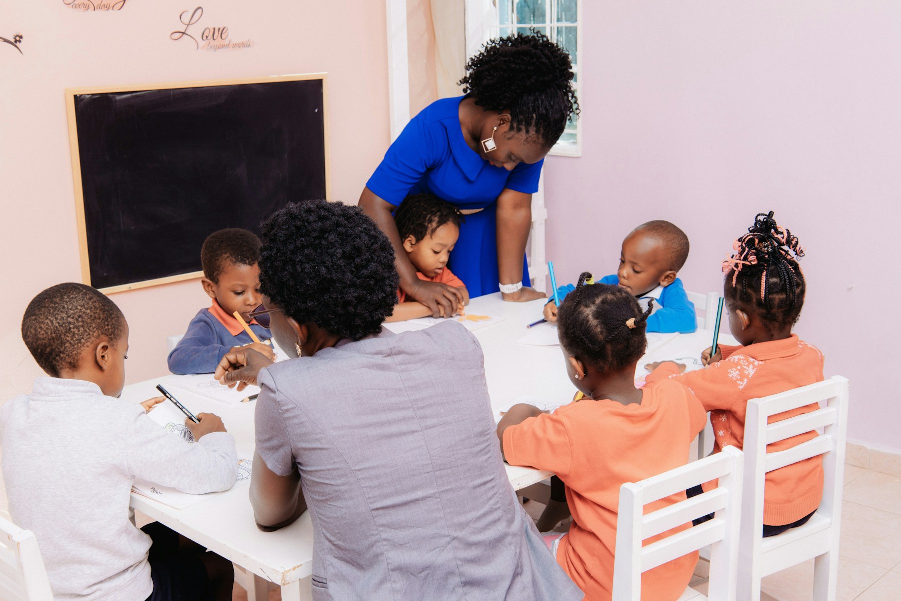 A teacher sits with children as they draw together.