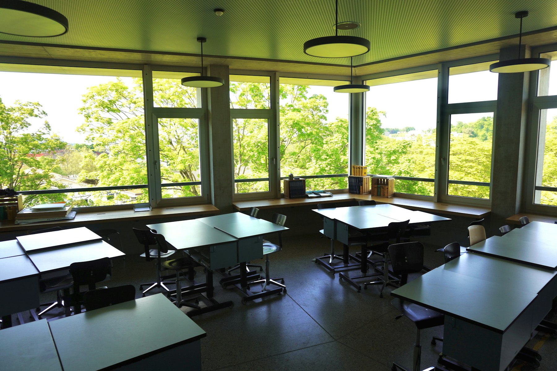 An unoccupied classroom with desks beside wide windows.